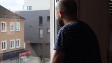 Pencereden dışarı bakan tişörtlü üzgün genç adam..