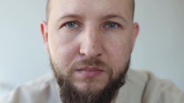 Sakallı genç adam gülümseyerek gözlük takıyor..