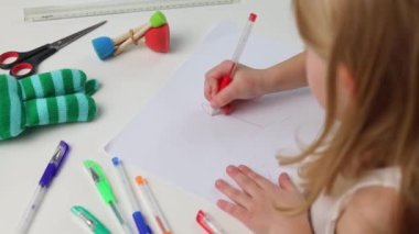Çocuk kız masada oturan bir kalemle resim çizer. Üst görünüm, düz uzanma.