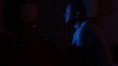 Gece geç saatte karanlık bir odada televizyon izleyen bir adam.