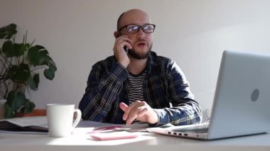 Ofisteki masada oturan gözlüklü adam telefonla konuşuyor.