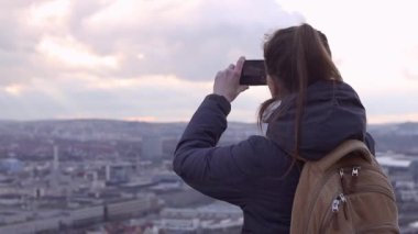 Genç bir kadın telefonuyla şehrin panoramasının fotoğrafını çekiyor..