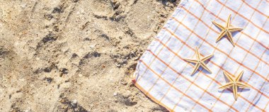 Kumlu bir sahilde, yatak örtüsünde altın denizyıldızı. Üst manzara, düz yatış. Pankart.