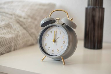 Retro alarm saati yatağın yanındaki beyaz komodinin üzerinde duruyor..