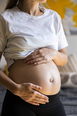 Hamile genç bir kadın bebeğinin karnını tutmasını dinliyor..