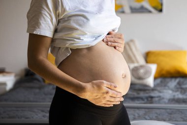 Hamile genç bir kadın karnını tutarak bebeğin itmesini dinliyor..