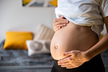 Hamile genç bir kadın karnını tutarak bebeğin itmesini dinliyor..