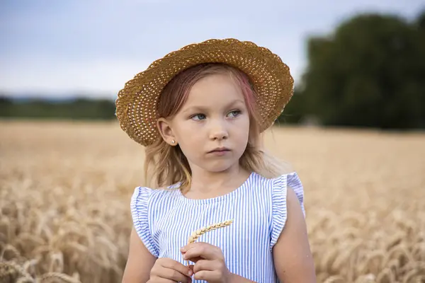 Şapkalı kız çocuğu buğday tarlasının arka planında duruyor..