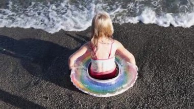 Deniz kıyısında şişme yüzüklü küçük bir kız oynuyor.