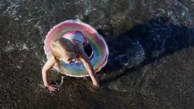 Deniz kıyısında şişme yüzüklü küçük bir kız oynuyor.