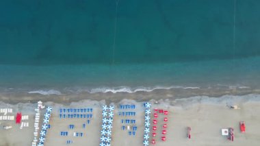 Deniz kıyısında güneşli şezlongları ve güneşliği olan boş bir sahil, insansız hava aracının manzarası.