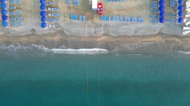 Deniz kıyısında güneşli şezlongları ve güneşliği olan boş bir sahil, insansız hava aracının manzarası.