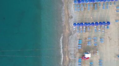Deniz kıyısında güneşli şezlongları ve güneşliği olan boş bir sahil, insansız hava aracının manzarası.