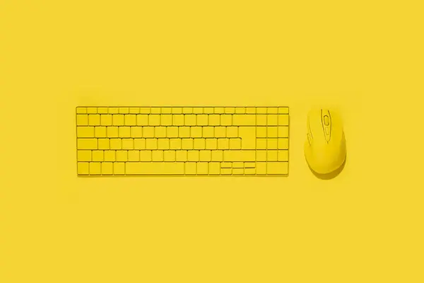 Yellow keyboard and yellow computer mouse on a yellow background. Top view, flat lay.