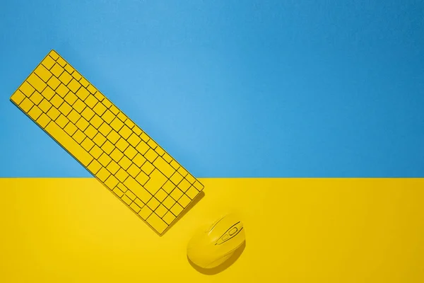 Yellow keyboard and yellow computer mouse on a yellow-blue background. Top view, flat lay.