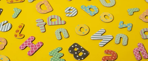 Many multi-colored letters of the alphabet on a yellow background. Top view, flat lay. Banner.