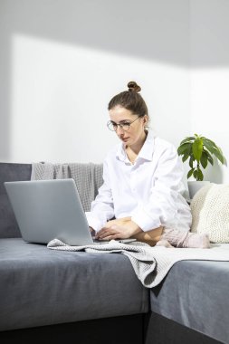 Young woman in glasses working with laptop sitting on sofa