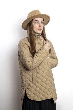 Beyaz bir duvarın arkasında şapkası olan ceketli güzel bir kadın.