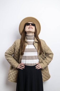 Şapkalı genç bir kadın beyaz bir duvarın arkasına bakıyor.