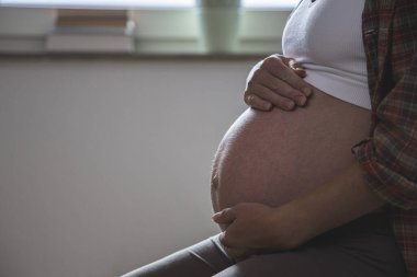 Hamile genç bir kadın karnına sarılıyor..