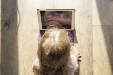 Yerde yatan küçük bir kız çocuğu tablete bakıyor. Üst manzara, düz uzanma.