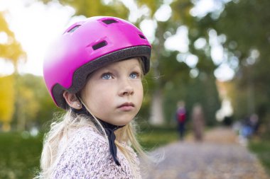 Sad child girl in a pink helmet in the park.