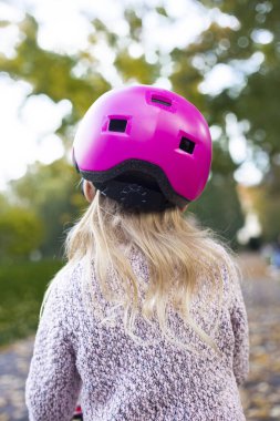Child girl in a pink helmet from behind in the park.