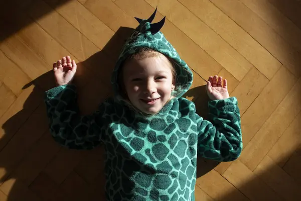 Smiling child girl in dinosaur costume lies on the floor. Top view, flat lay.