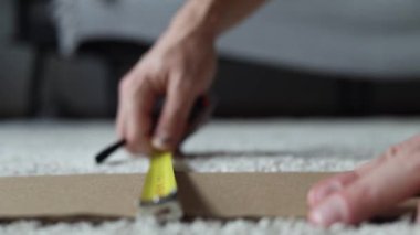 Adam bir karton yaprağının genişliğini mezura ile ölçer.