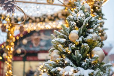 Oyuncak toplarıyla süslenmiş Noel ağacı ve arka planda kar ile süslenmiş bir çelenk.