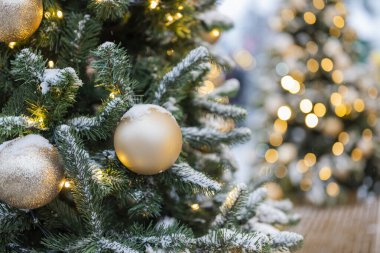 Oyuncak toplarıyla süslenmiş Noel ağacı ve arka planda kar ile süslenmiş bir çelenk.