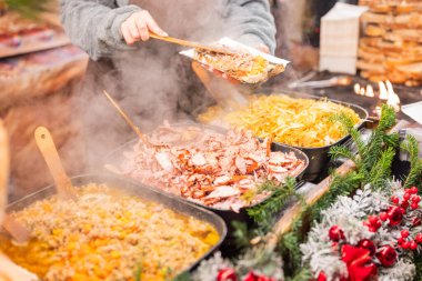 Satıcı, şehir merkezindeki Krakow Polonya 'daki Noel pazarında et ve sosis kızartıyor.