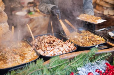 Satıcı, şehir merkezindeki Krakow Polonya 'daki Noel pazarında et ve sosis kızartıyor.