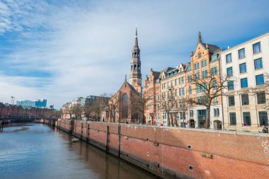 5 Eylül 2022, Hamburg, Almanya, Speicherstadt bölgesindeki nehirde tuğladan evler ve St. Katharinen Kilisesi manzaralı bir kanal.
