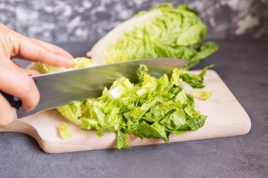 Aşçı kız yemek pişirmek için yeşil marul yaprağını bıçakla kesiyor.