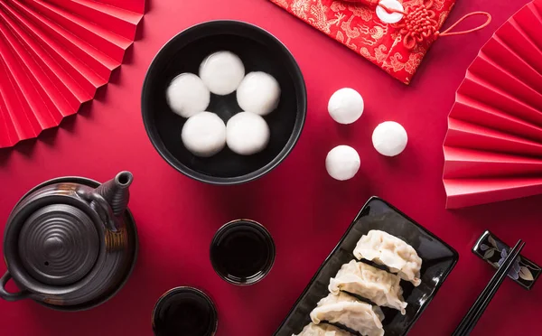 stock image Tang Yuan(sweet dumplings balls), a traditional cuisine for Mid-autumn, Dongzhi (winter solstice ) and Chinese new year with plum flower and tea on red background.