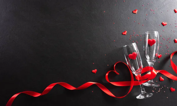 Valentine's day and love concept made from champagne glasses and red hearts on black wooden background.