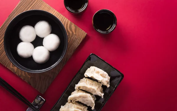 stock image Tang Yuan(sweet dumplings balls), a traditional cuisine for Mid-autumn, Dongzhi (winter solstice ) and Chinese new year with plum flower and tea on red background.