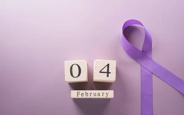 Purple ribbon and wooden calendar on pastel paper background for supporting World Cancer Day campaign on February 4.