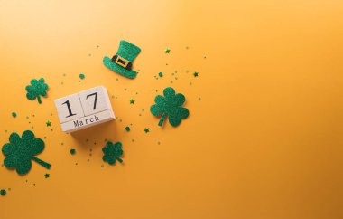 Happy St Patrick's Day decoration concept made from shamrocks ( clover leaf), wooden calendar and leprechaun hat on yellow background.