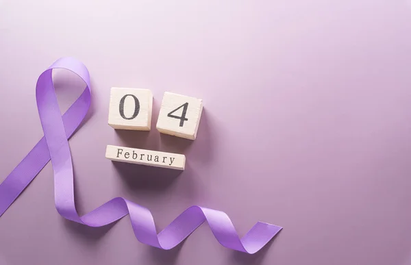 Purple ribbon and wooden calendar on pastel paper background for supporting World Cancer Day campaign on February 4.