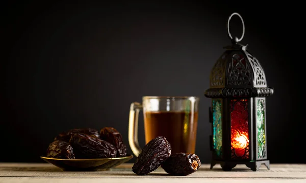 Ramadan food and drinks concept.  Ramadan Lantern with arabian lamp, wood rosary, tea, dates fruit and lighting on a wooden table with dark background.