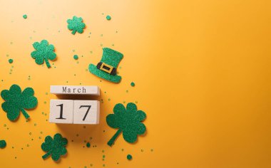 Happy St Patrick's Day decoration concept made from shamrocks ( clover leaf), wooden calendar and leprechaun hat on yellow background.