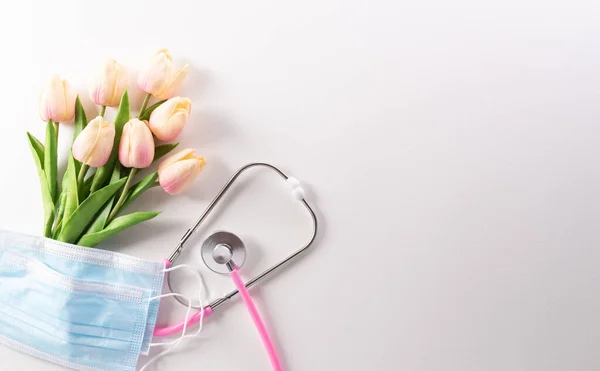 Top view of doctor stethoscope, medical mask and flowers on white background. International nurse day and medical concept.