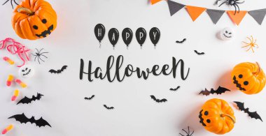 Cadılar Bayramı süslemeleri balkabağı, kağıt yarasalar, siyah örümcek ve pastel turuncu arkaplandaki yazı..