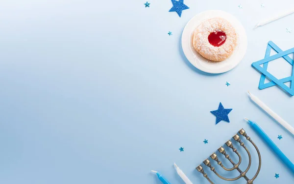 Jewish holiday Hanukkah concept. Top view of sweet donuts, menorah and candles on blue background.