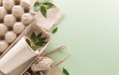 Dünya Çevre Günü, yeşile dönün, geri dönüşüm, toprak günü ve eko konsepti, farklı kağıt atık malzemeleri ve pastel arka planda bitki.