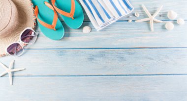 Yaz tatili, seyahat ve tatil konsepti. Güneş gözlüğü, denizyıldızı, plaj şapkası, terlik ve deniz kabuğu pastel mavi ahşap arka planda..