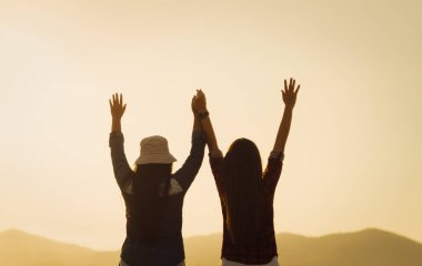 Kadınlar gün batımında dağın önünde el ele tutuşarak eğleniyorlar. Mutluluk, başarı, dostluk ve toplum kavramları.