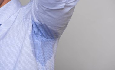 Hiperhidrozlu terleyen yakın plan bir adam. Giysilerinde gri arka planda ter lekesi olan bir adam. Sağlık hizmetleri kavramı.